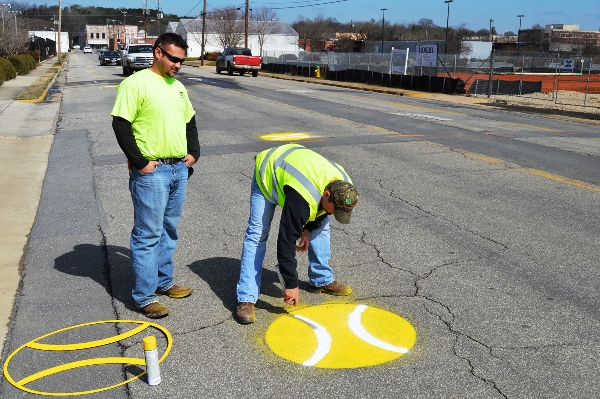 Left to right: Russ Atkins and Tim Chambers paint tennis balls on West Third Street on Friday as part of the March Into Tennis celebration.